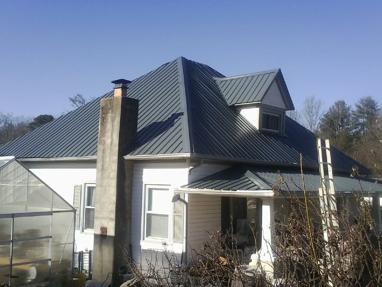 Dark blue standing seam metal roof on a white farmhouse with dormer — Slate & Tile Roof Repair by Roofing Brothers in Norfolk